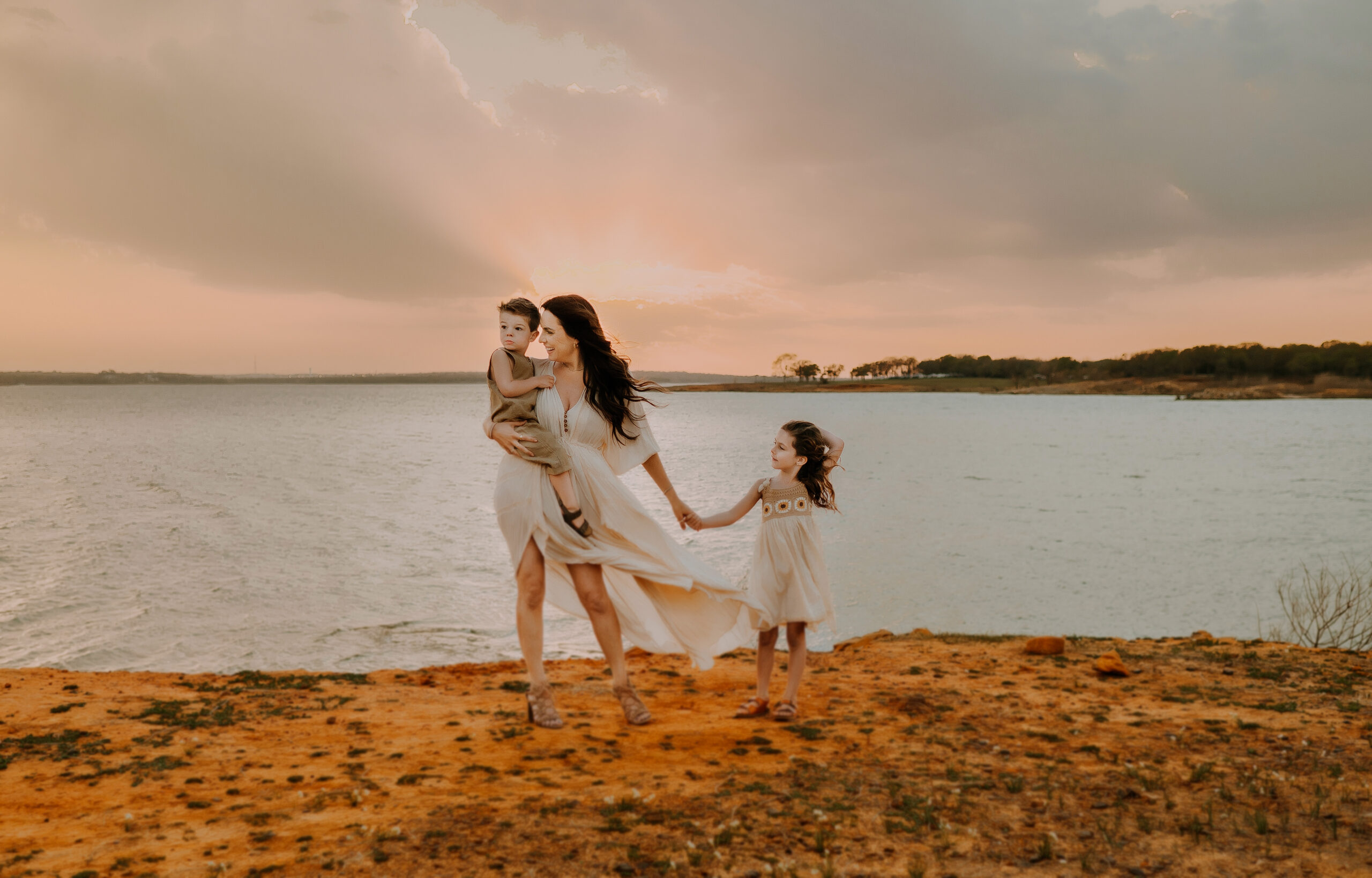 A mom and her two kids are standing near the waters edge at Murrell Park while the wind blows their hair.