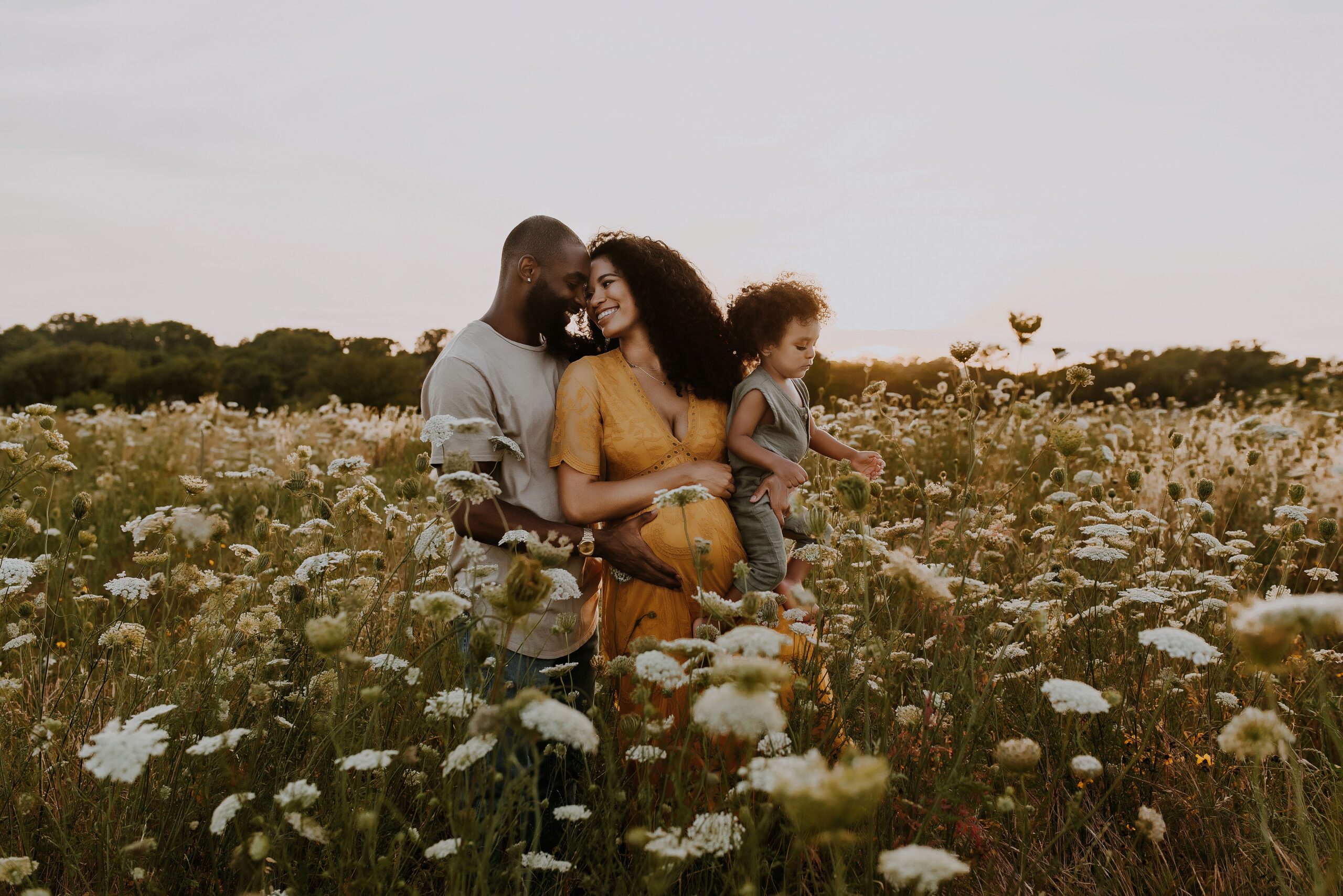 A family of three are giggling together in a field of white flowers near Boy Scout Hill in Dallas, Texas