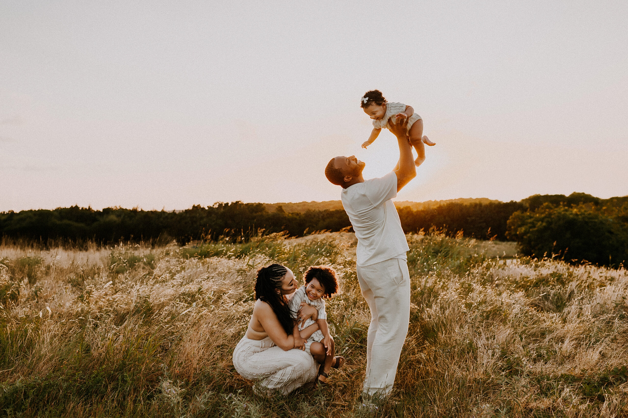 A family of four are standing in a field at Arbor Hills Nature Preserve in Plano, Texas while dad holds baby up in the air and mom tickles her son.