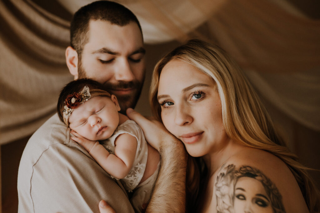 Mom, dad and newborn baby snuggled together in Dallas newborn studio 