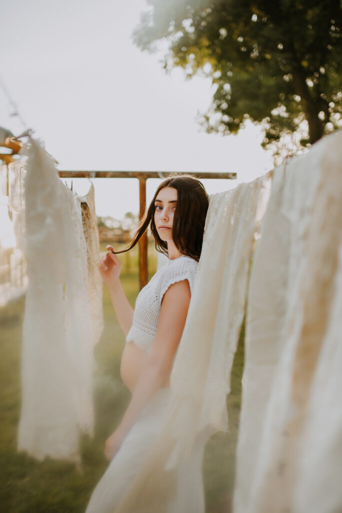 A mom holding her hair and standing next to a clothes line at the little glass shack in howe, tx