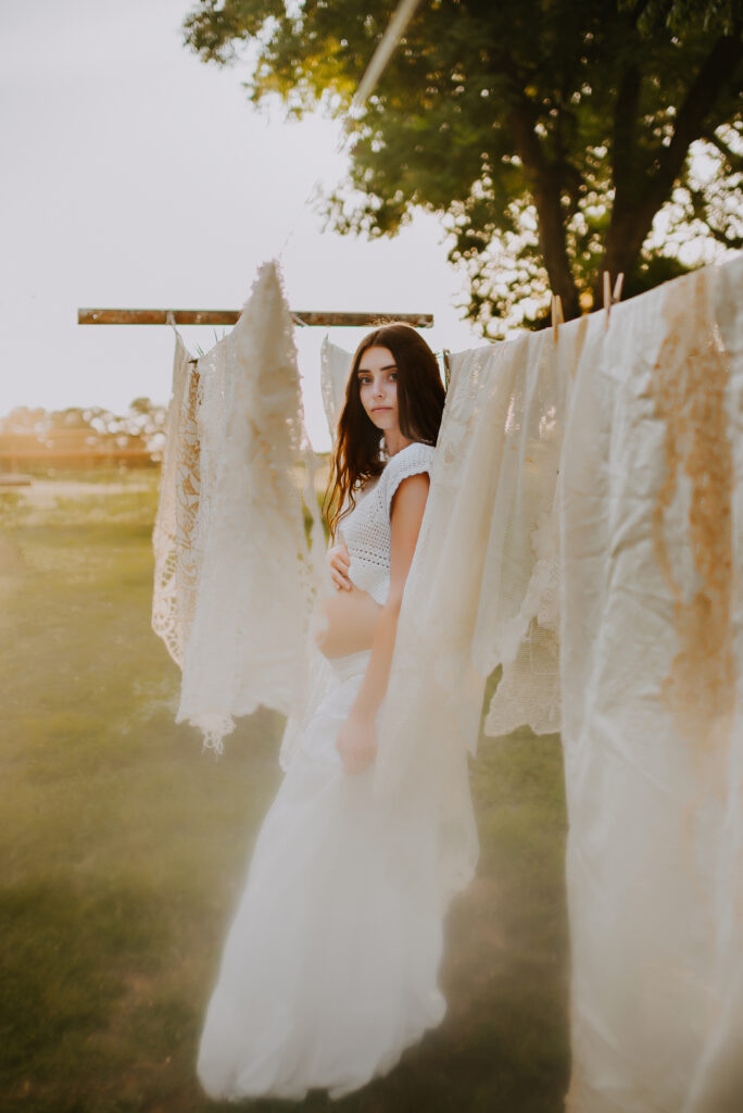 A mom standing next to a clothes line holding her pregnant belly in a two piece boho inspired dress in Howe, TX