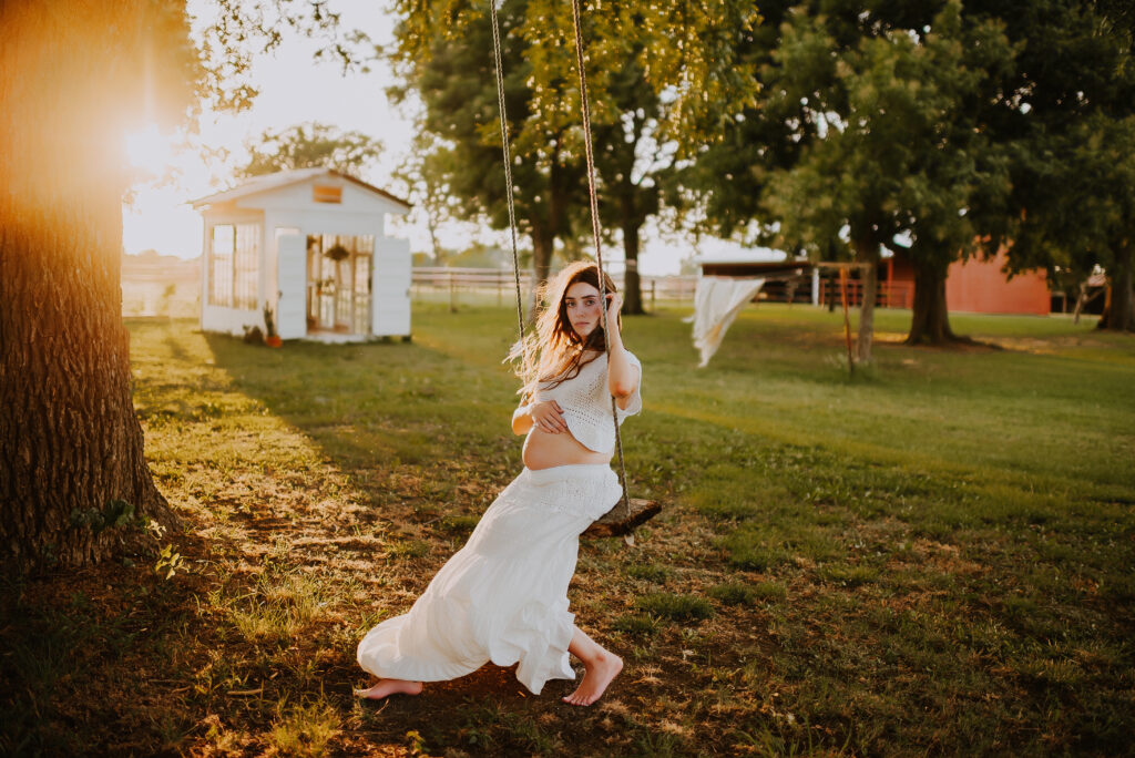A mom swinging on an old tree swing holding her belly at the little glass shack in howe, texas