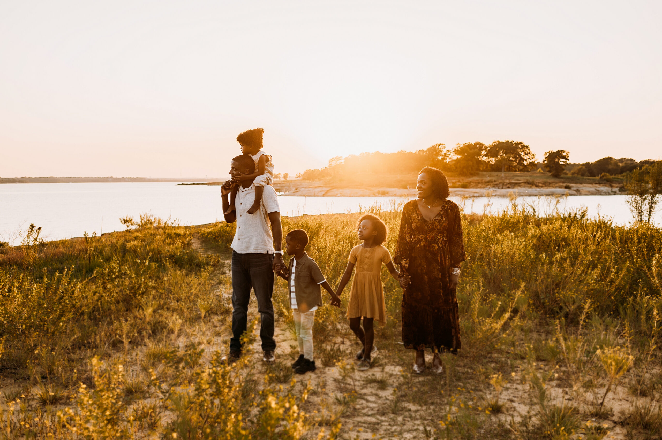 A family of five is standing on the shores of grapevine lake at sunset holding hands at murrell park in flower mound, tx