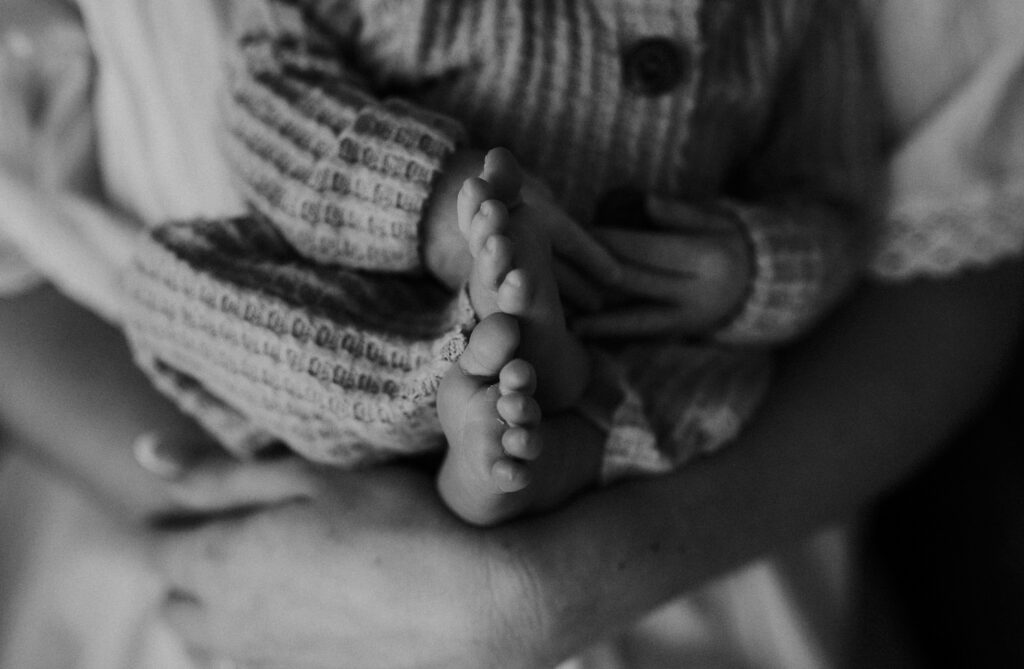 A black and white image of tiny baby feet curled into a little ball in a boho studio in fort worth, texas