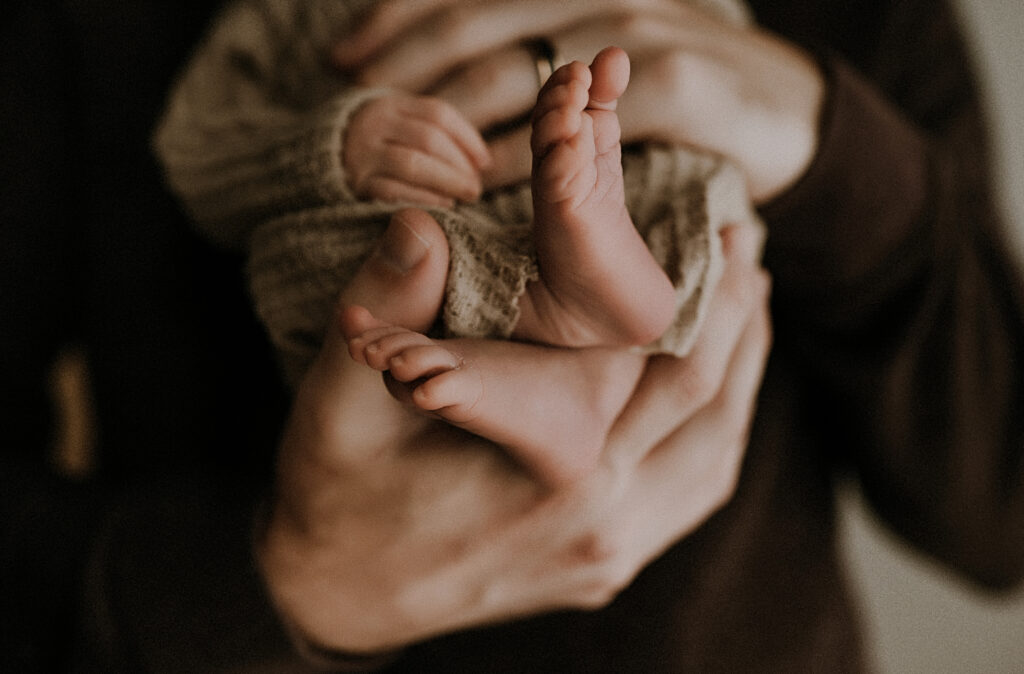 Dad embracing baby's tiny hands and feet in a fort worth, texas studio