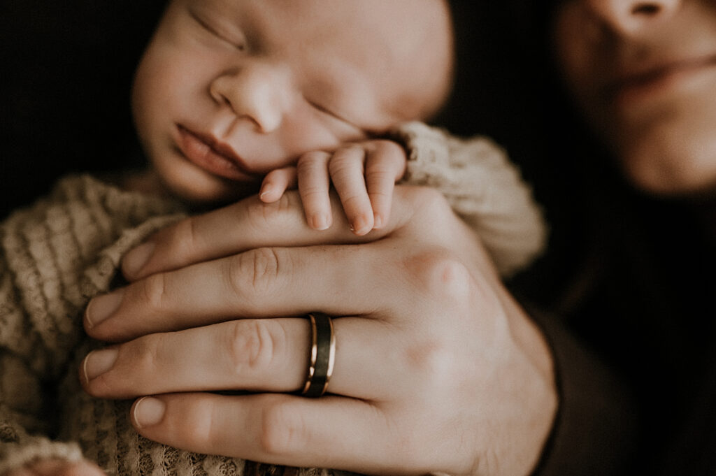 A close up of dad holding baby with his big hands as baby rests on his own little hand in fort worth, texas