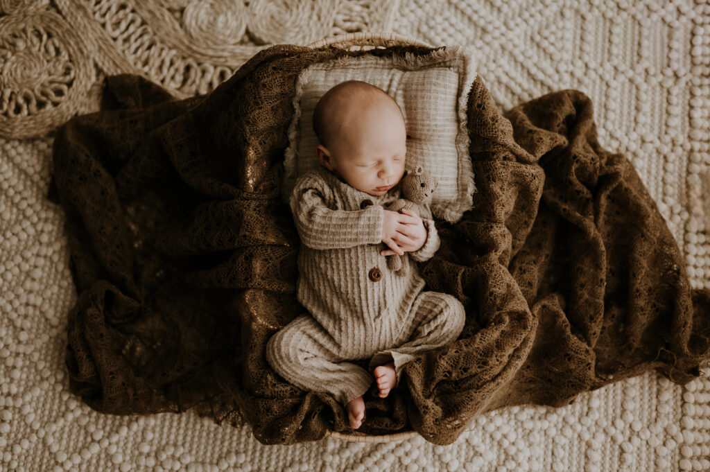 A baby holding a tiny teddy bear in a little basket sleeping in fort worth, texas