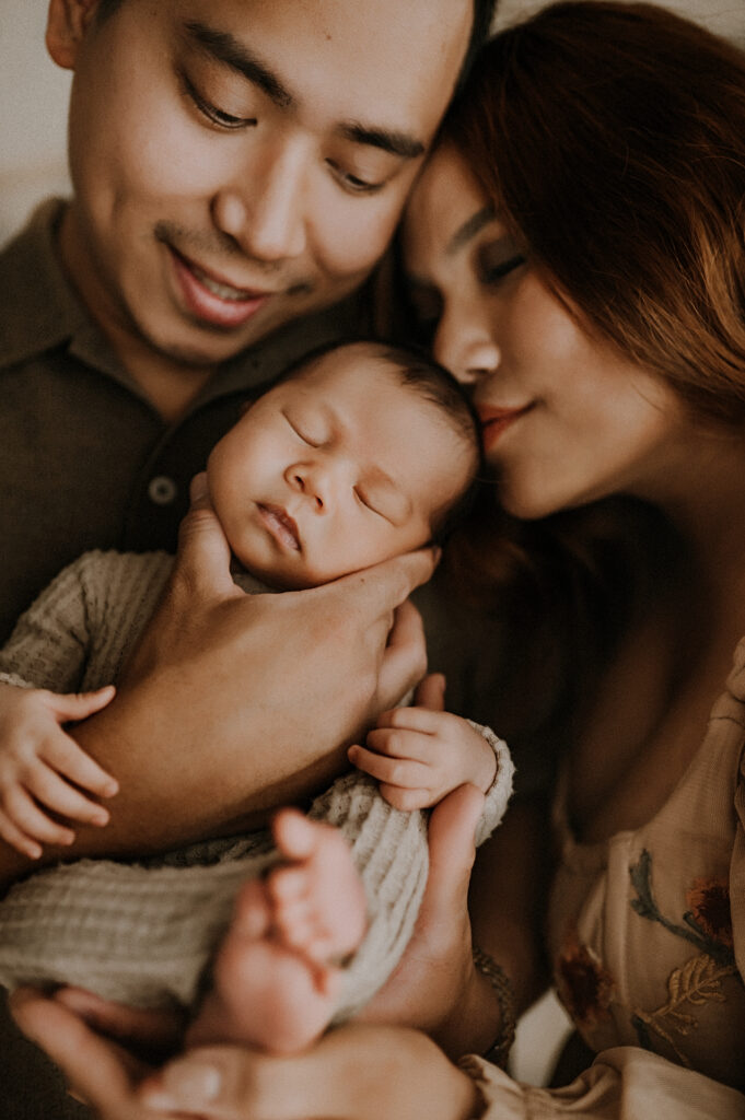 A mom putting her nose to her baby's sleeping head while dad holds him in his arms.