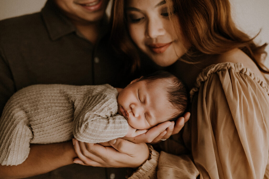 A Mom looking down at her newborn son sleeping in his dad's arms in fort worth, texas