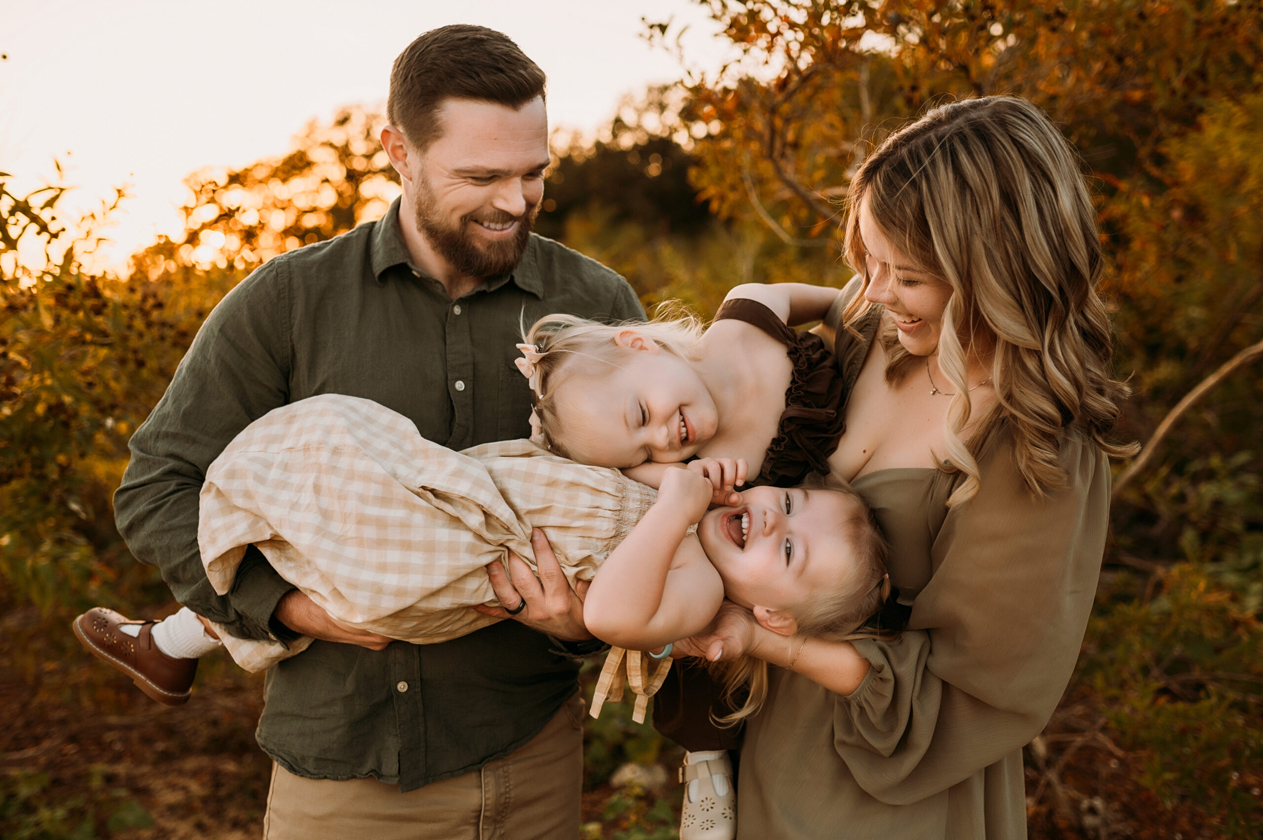 A family of four are cuddling and laughing as mom hold the two twin girls at murrell park in flower mound, texas