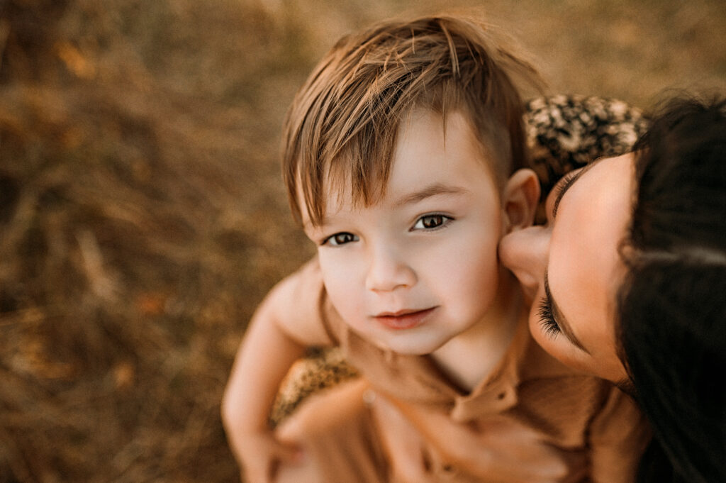 A mom is sticking her nose on her sons cheek as he looks up at the sky in plano, texas