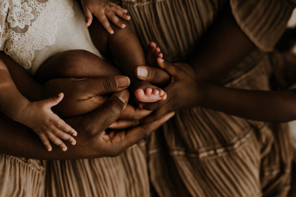 A mom, dad and toddler girl all hold little baby's tiny toe in fort worth, texas
