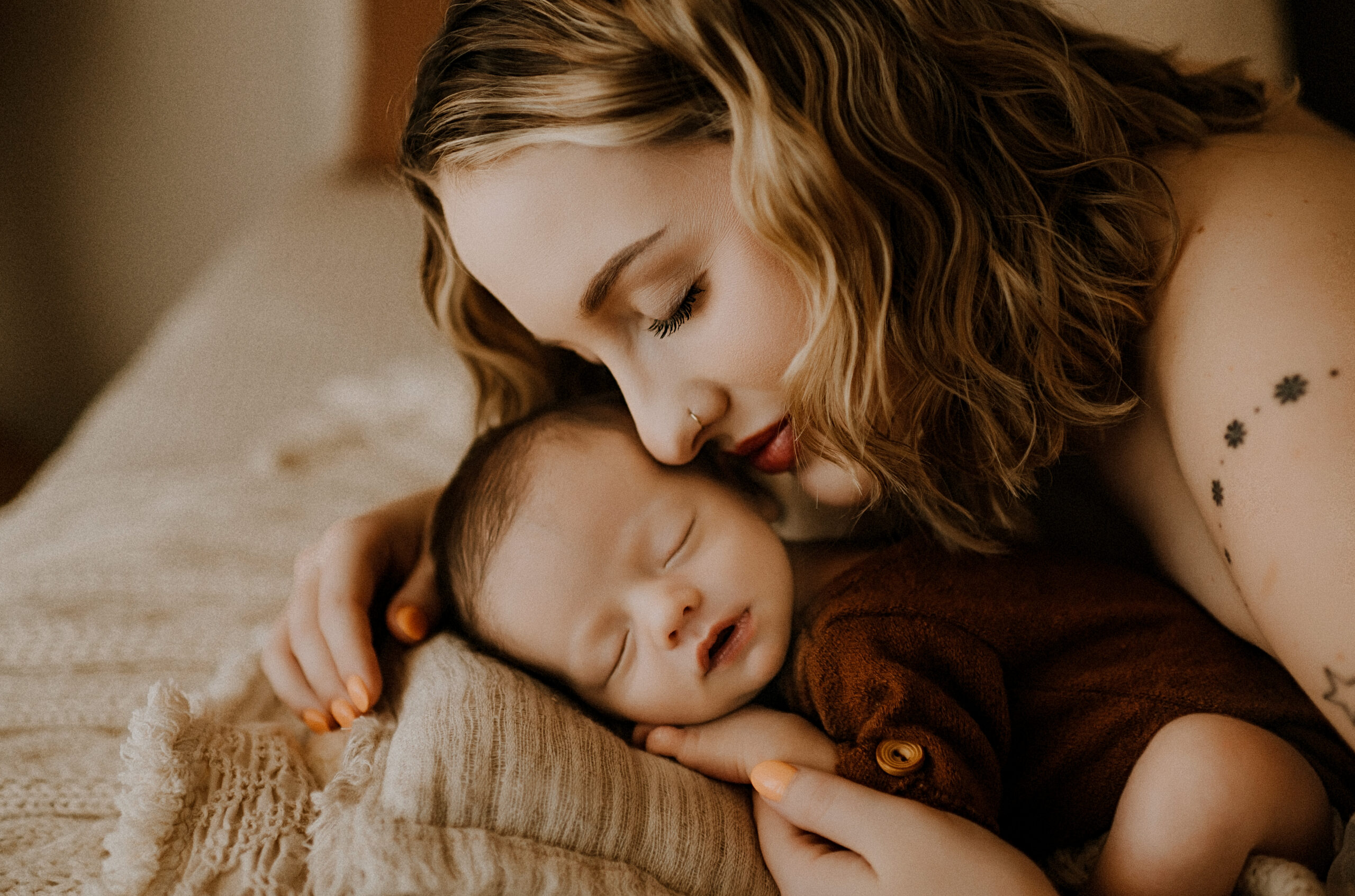 a mom is laying on a bed with her nose on her newborn baby's cheek at a fort worth photography studio