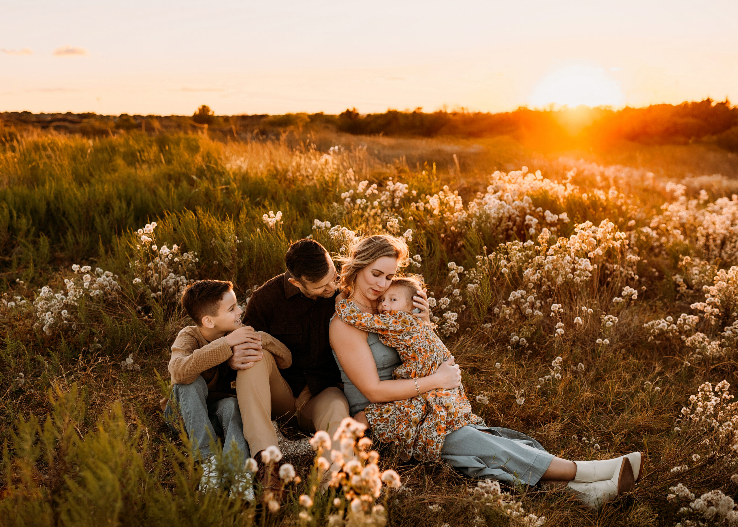 A family of four are sitting around some wispy wildflowers and cuddling in Plano, Texas